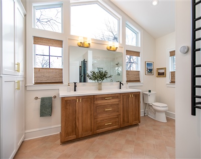 Bright bathroom with a large window, wooden vanity, tile flooring, and a mirror reflecting a potted plant.