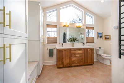 Bright bathroom with a large window, wooden vanity, tile flooring, and a mirror reflecting a potted plant.