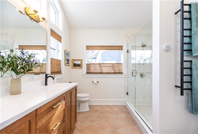 Bright and airy bathroom featuring a wooden vanity, two mirrors with upper lighting, a glass shower stall, and white walls with two wooden shelves.