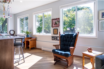 Sunny home office with three large windows, a traditional blue leather armchair, wooden desk, and hardwood floors, bathed in natural light.