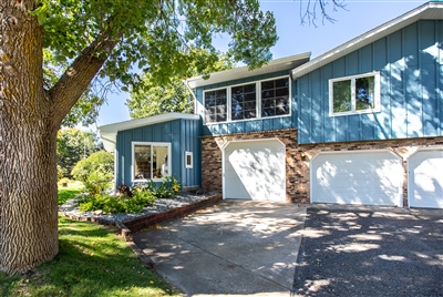 A split-level house with teal siding and white trim, featuring two garages and landscaped surroundings, under a clear sky.