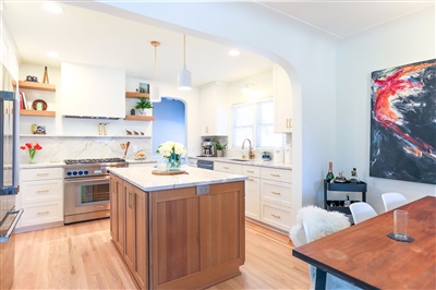 Spacious kitchen with a central island, white cabinets, wooden floors, and modern appliances, accented by a colorful artwork on the wall.