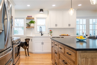 A well-lit kitchen featuring white cabinets, a farmhouse sink, wooden countertops, and a black dog by the island.