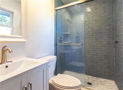 Modern bathroom with a white vanity, marble countertop, and a glass shower enclosure featuring blue subway tile walls.